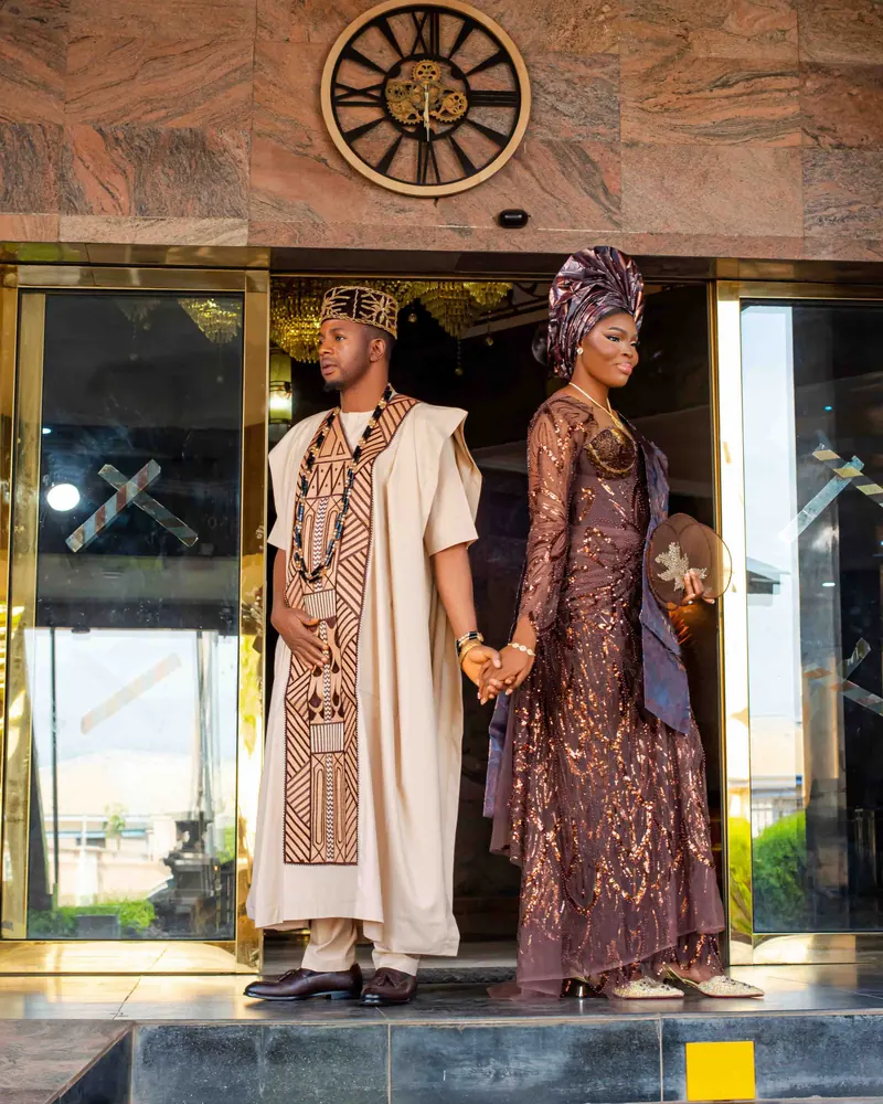 A couple in traditional attire hold hands at the entrance of a building