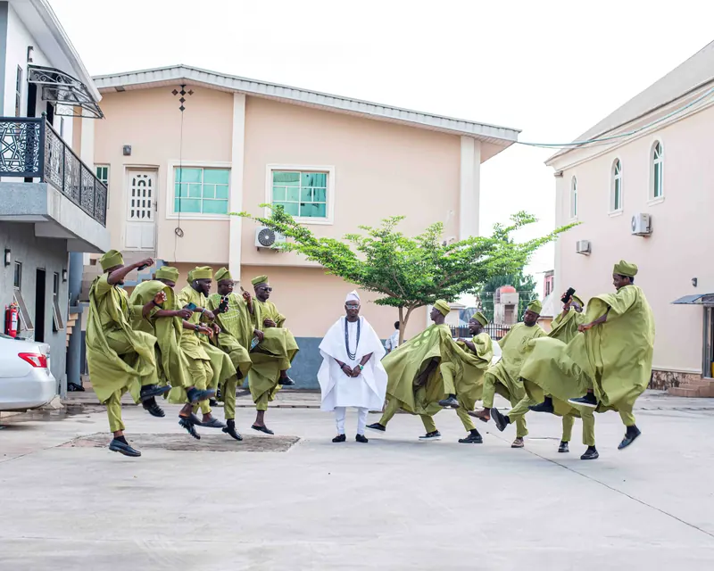 Dancers in matching olive-green agbada perform in a street